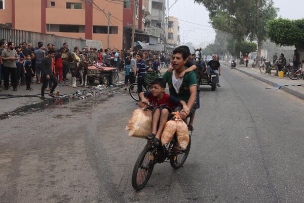جوانان در حالی که در رفح در جنوب نوار غزه دوچرخه سواری می کنند کیسه های نان حمل می کنند.  - اسپوتنیک ایران  
