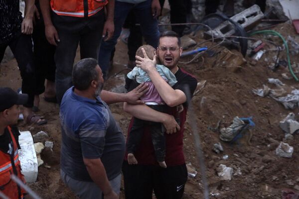 یک مرد فلسطینی در حالی که کودک مرده‌ای را در آغوش گرفته، گریه می‌کند. جسد این کودک در زیر آوارهای یک ساختمان ویران شده در پی حملات هوایی اسرائیل در اردوگاه آوارگان نصیرات در مرکز نوار غزه، پیدا شد. سه‌شنبه 31 اکتبر 2023. - اسپوتنیک ایران  