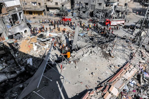 مردم در حالی که امدادگران در جستجوی قربانیان و بازماندگان در آوارهای ساختمانی هستند که در 31 اکتبر 2023 در بحبوحه نبردهای بین اسرائیل و جنبش فلسطینی حماس در رفح در جنوب نوار غزه هدف بمباران اسرائیل قرار گرفته، ایستاده اند. - اسپوتنیک ایران  