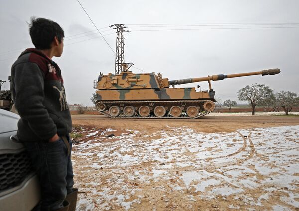 یک کودک در 12 فوریه 2020 در شهر بنیش در استان ادلب در شمال غربی سوریه، در نزدیکی مرز سوریه و ترکیه به توپ خودکششی 155 میلی متری ارتش ترکیه نگاه می کند که وارد سوریه شده است - اسپوتنیک ایران  