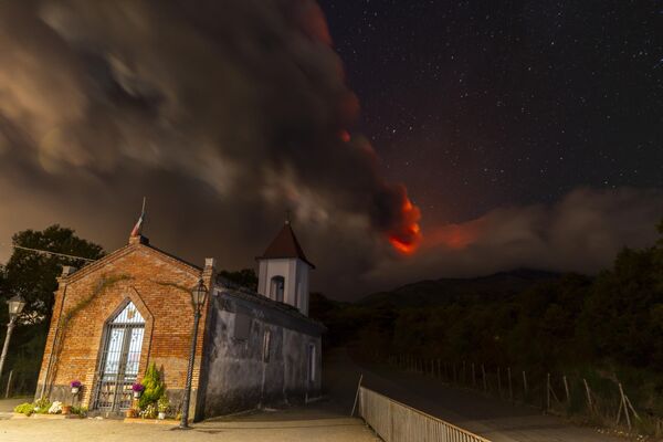 فوران دود از کوه آتشفشان اتنا، از  پشت کلیسای Magazzeni در نزدیکی روستای سنت آلفیو، در شمال کاتانیا، سیسیل، جنوب ایتالیا دیده می‌شود. 12 نوامبر 2023 - اسپوتنیک ایران  