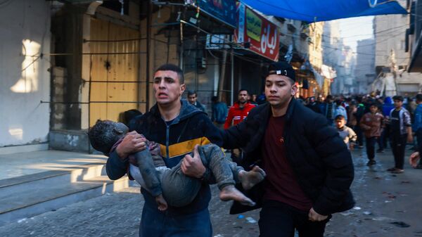 یک فلسطینی پس از بمباران مجدد شهر رفح، در جنوب نوار غزه توسط اسرائیل، پسربچه مجروحی را حمل می کند. - اسپوتنیک ایران  
