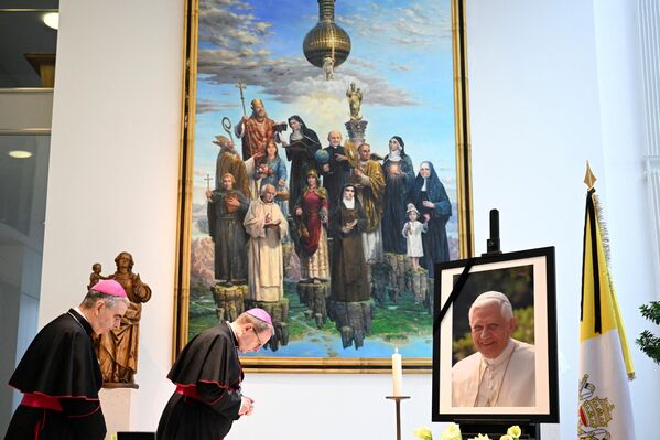 رئیس کنفرانس اسقفان آلمان، اسقف گئورگ باتزینگ (راست) و اسقف اعظم و نونسیه حواری در آلمان، نیکولا اتروویچ، قبل از امضای کتاب تسلیت در نونسیه حواری به آلمان، در مقابل تصویر پاپ  فقید بندیکت شانزدهم ادای احترام کردند. در برلین، در 2 ژانویه 2023. - اسپوتنیک ایران  