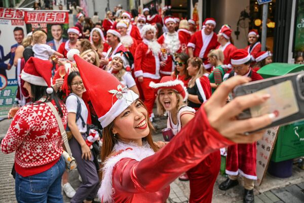 زنی که لباس بابا نوئل پوشیده است در جریان مراسم سالانه SantaCon در هنگ کنگ سلفی می گیرد. 9 دسامبر 2023 - اسپوتنیک ایران  