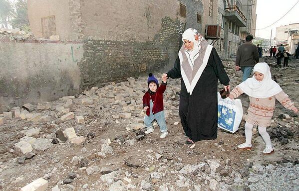 یک زن عراقی در 17 دسامبر به فرزندان خود کمک می کند تا از روی آوارهای باقی مانده پس از حملات هوایی شبانه آمریکا و انگلیس به بغداد عبور کنند. - اسپوتنیک ایران  