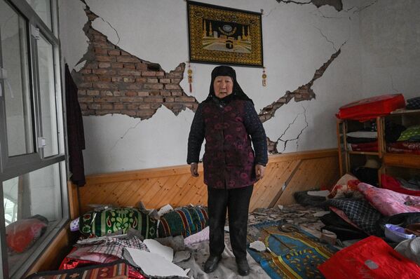 یک زن در 19 دسامبر 2023 خسارت وارده به خانه خود را پس از زلزله در داهجیا، شهرستان جیشیشان در استان گانسو شمال غربی چین نشان می دهد. - اسپوتنیک ایران  
