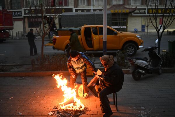 مردم پس از زلزله در داهجیا، شهرستان جیشیشان در استان گانسو شمال غربی چین در 19 دسامبر 2023  در خیابانی آتش روشن کرده و خود را گرم می کنند. - اسپوتنیک ایران  