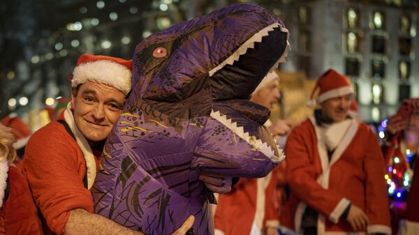 Мужчина в костюме Санта-Клауса обнимает свой надувной костюм динозавра в Лондоне, Великобритания - اسپوتنیک ایران  