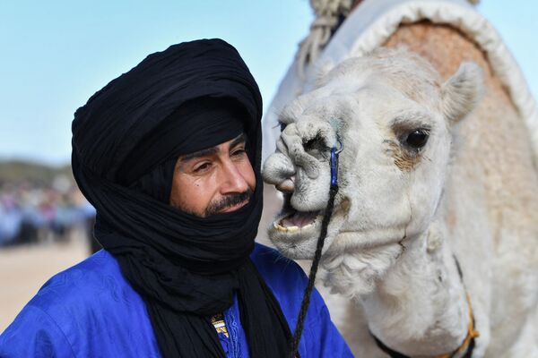 مجری با لباس سنتی در حین نمایش در آغاز جشنواره بین المللی صحرا در دوز، در جنوب تونس، کنار شتر ایستاده است. 27 دسامبر 2023 - اسپوتنیک ایران  