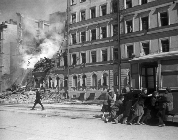 جنگ بزرگ میهنی 1941-1945 . دفاع از لنینگراد.   ساکنان این شهر محاصره شده پس از حمله هوایی فاشیست ها یک واگن تراموا را از جلوی  خانه ای ویران شده جابجا می کنند. - اسپوتنیک ایران  