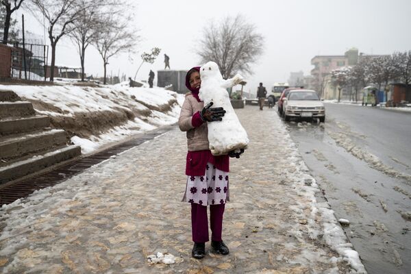 یک دختر افغان در 19 فوریه 2024 یک آدم برفی را در مسیر سنگفرش پر از برف در کابل حمل می کند.  - اسپوتنیک ایران  