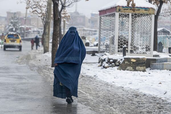 یک زن برقع پوش افغان در 19 فوریه 2024 از کنار خیابانی از کنار گورستان پر از برفی در کابل عبور می کند. - اسپوتنیک ایران  