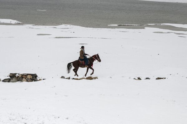 یک مرد افغان در 19 فوریه 2024 سوار بر اسب از دریاچه پر برف قرغه در حومه کابل عبور می کند.  - اسپوتنیک ایران  