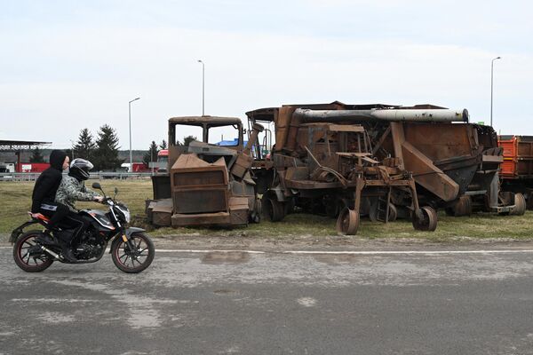 مردم با موتورسیکلت از کنار خودروهای کشاورزی تخریب شده اوکراینی عبور می کنند که توسط کشاورزان اوکراینی به گذرگاه مرزی کراکوتس در مرز اوکراین و لهستان منتقل شده اند. - اسپوتنیک ایران  