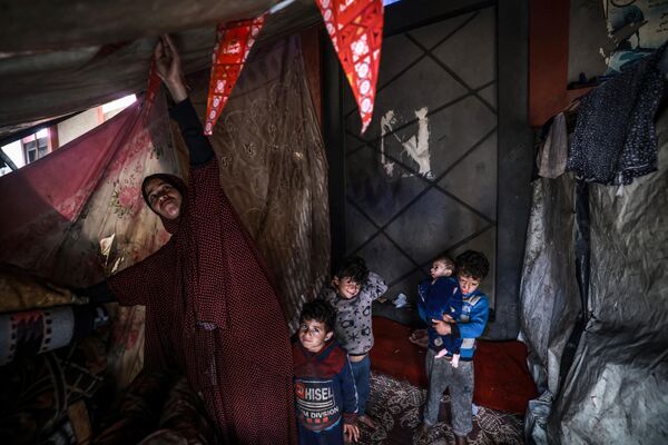 یک زن آواره فلسطینی به همراه کودکان در بحبوحه نبردهای جاری بین اسرائیل و گروه شبه نظامی حماس در چادر خود در اردوگاهی در کنار خیابانی در رفح در 14 مارس 2024. درگیری اسرائیل و حماس که از 7 اکتبر آغاز شده است، منجر به تلفات انبوه غیرنظامیان شده، مناطق وسیعی را به یک زمین بایر پر از آوار تبدیل کرده و هشدارهایی را درباره قحطی قریب الوقوع در این سرزمین فلسطینی با 2.4 میلیون نفر جمعیت به دنبال داشته است. - اسپوتنیک ایران  