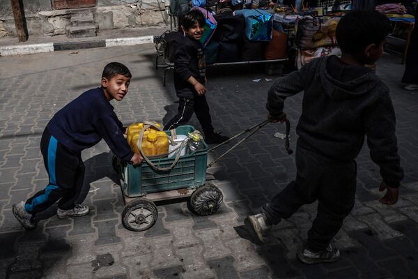 کودکان آواره فلسطینی در 14 مارس 2024، در میان نبردهای جاری بین اسرائیل و گروه شبه نظامی حماس، در اردوگاهی در کنار خیابانی در رفح عکس می گیرند. درگیری اسرائیل و حماس که از 7 اکتبر آغاز شده است، منجر به تلفات انبوه غیرنظامیان شده، مناطق وسیعی را به یک زمین بایر پر از آوار تبدیل کرده و هشدارهایی را درباره قحطی قریب الوقوع در سرزمین فلسطینی با 2.4 میلیون نفر جمعیت به دنبال داشته است. - اسپوتنیک ایران  