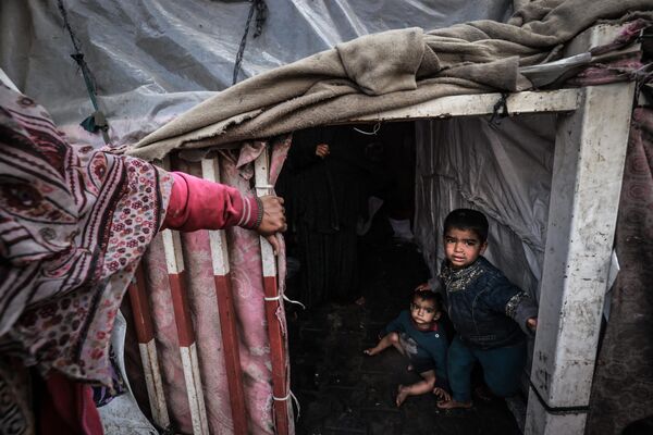 کودکان آواره فلسطینی در 14 مارس 2024، در میان نبردهای جاری بین اسرائیل و گروه شبه نظامی حماس، در اردوگاهی در کنار خیابانی در رفح عکس می گیرند. درگیری اسرائیل و حماس که از 7 اکتبر آغاز شده است، منجر به تلفات انبوه غیرنظامیان شده، مناطق وسیعی را به یک زمین بایر پر از آوار تبدیل کرده و هشدارهایی را درباره قحطی قریب الوقوع در این سرزمین فلسطینی با 2.4 میلیون نفر جمعیت به دنبال داشته است. - اسپوتنیک ایران  