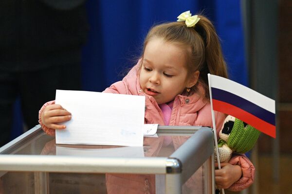 در جریان انتخابات ریاست جمهوری روسیه، یک دختر یک برگه رای را در صندوق رای در یک شعبه رای در سفارت روسیه در مینسک می اندازد - اسپوتنیک ایران  