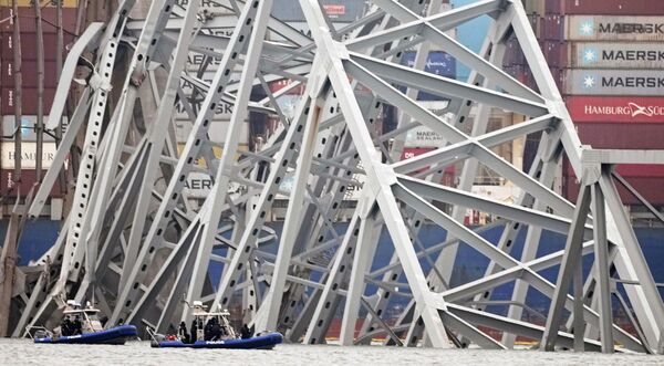 قایق های غواصی پلیس در اطراف یک کشتی باری کار می کنند که پس از برخورد این کشتی با پل در چهارشنبه، 27 مارس 2024، در بالتیمور، زیر بخشی از ساختار پل فرانسیس اسکات کی گیر کرده است. - اسپوتنیک ایران  