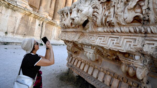 یک بازدیدکننده از نقش برجسته‌های موجود در مجموعه معبد شهر باستانی بعلبک لبنان عکس می‌گیرد. - اسپوتنیک ایران  
