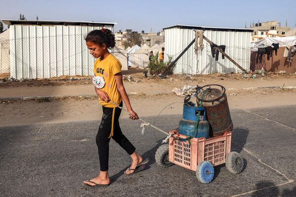 دختری در 23 آوریل 2024 در بحبوحه درگیری های جاری در خاک فلسطین بین اسرائیل و گروه شبه نظامی حماس، گاری پر از سیلندرهای گاز را در امتداد خیابانی در رفح در جنوب نوار غزه می کشد. - اسپوتنیک ایران  
