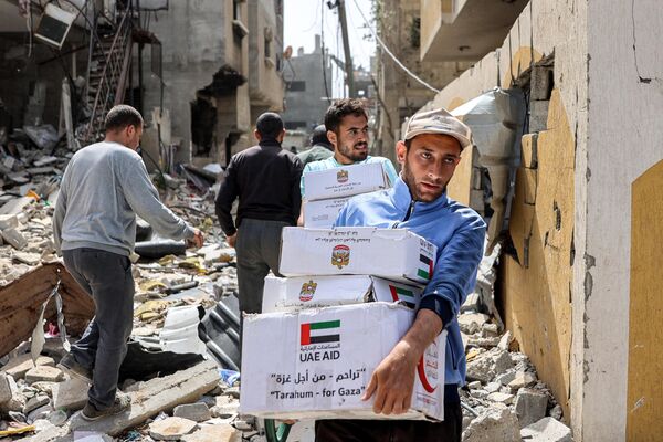 مردان با بسته‌های کمک‌های بشردوستانه که در 23 آوریل 2024 در بحبوحه درگیری‌های جاری در خاک فلسطین بین اسرائیل و گروه شبه‌نظامی حماس جمع‌آوری شده ب، از مقابل ساختمان‌های آسیب‌دیده عبور می‌کنند. - اسپوتنیک ایران  