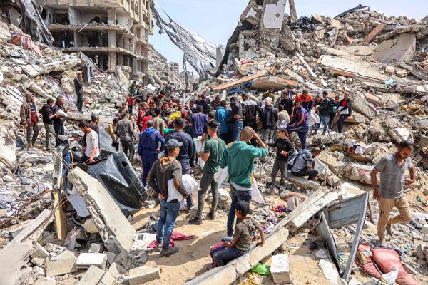 مردم در 23 آوریل 2024 در کنار یک ساختمان ویران شده در محل پرتاب کمک های بشردوستانه در شمال نوار غزه در بحبوحه درگیری های جاری در خاک فلسطین بین اسرائیل و گروه شبه نظامی حماس جمع می شوند. - اسپوتنیک ایران  