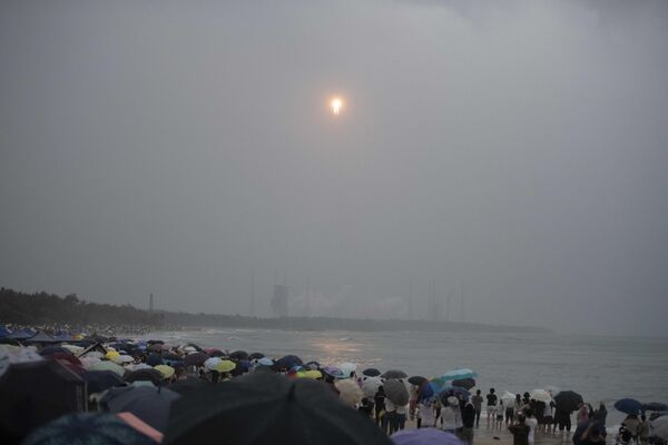 جمعیتی از ساحل تماشا می‌کنند که موشک لانگ مارس 5، حامل کاوشگر ماه ماموریت چانگ او-6، با بارش باران در مرکز پرتاب فضایی ونچونگ در استان هاینان در جنوب چین در 3 مه 2024 به آسمان بلند می‌شود. - اسپوتنیک ایران  