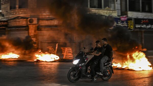 جوانان فلسطینی با موتور سیکلت در جریان یورش اسرائیل به شهر اشغالی جنین از کنار لاستیک های سوخته عبور می کنند. - اسپوتنیک ایران  