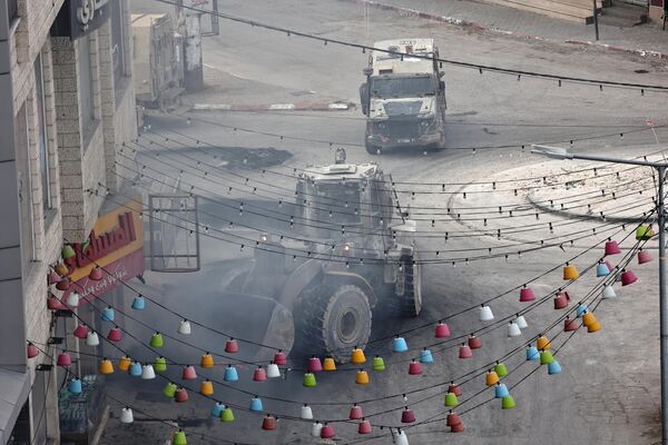 یک خودروی زرهی نیروهای اسرائیلی پشت یک بولدوزر در جاده اصلی جنین در جریان یک حمله مداوم به این شهر در کرانه باختری در 22 مه 2024 حرکت می کند. حمله اسرائیل به این شهر در روز 22 مه پس از کشته شدن هشت فلسطینی در روز قبلی ادامه یافت. - اسپوتنیک ایران  