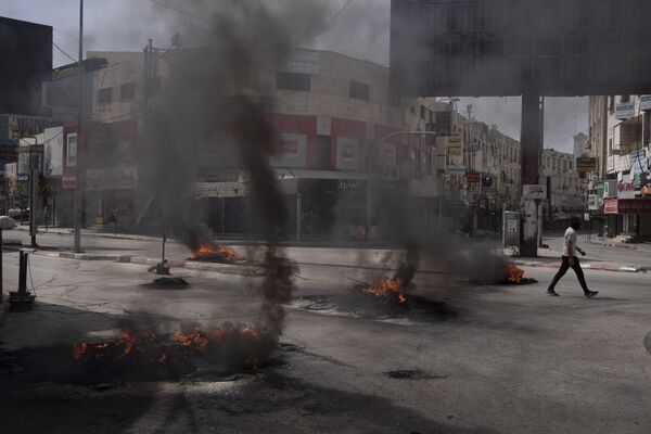 مردی فلسطینی در جریان درگیری با نیروهای اسرائیلی در شهر جنین در کرانه باختری، چهارشنبه 22 می 2024 از کنار لاستیک های سوخته عبور می کند. - اسپوتنیک ایران  