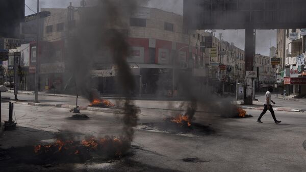 Палестинец проходит мимо горящих шин во время столкновений с израильскими войсками в городе Дженин на Западном Берегу, - اسپوتنیک ایران  