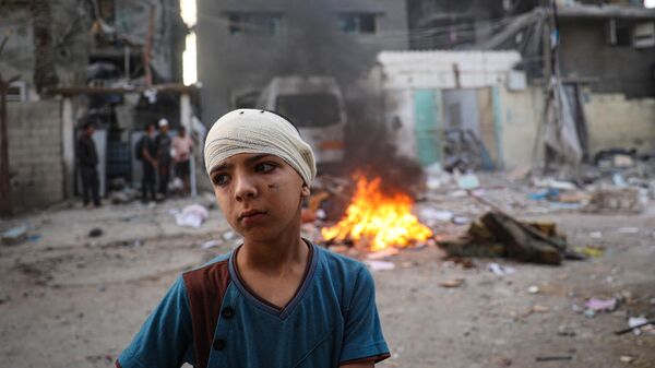 Раненый палестинский мальчик рядом с развалинами своего дома, который пострадал в результате израильской бомбардировки в районе Таль аль-Султан в Рафахе на юге Газы - اسپوتنیک ایران  