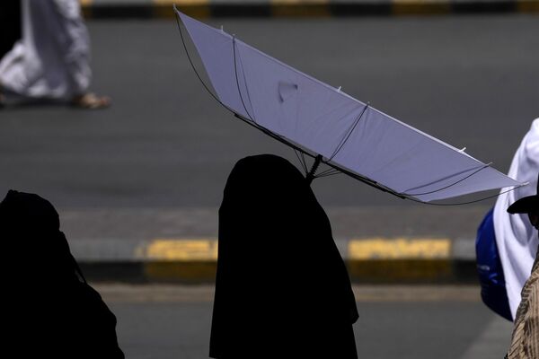 زنی هنگام خروج از مسجد الحرام، در حین زیارت سالانه حج در مکه، عربستان سعودی، پنج شنبه، 13 ژوئن 2024، چتر را برای محافظت از خود در برابر خورشید نگه می دارد. - اسپوتنیک ایران  