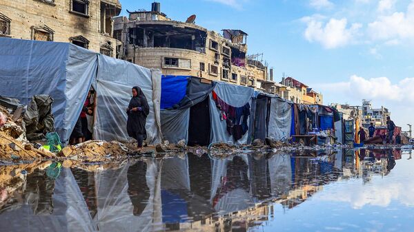 Палестинцы обходят лужу перед разрушенными зданиями и палатками в Хан-Юнисе, Палестина - اسپوتنیک ایران  