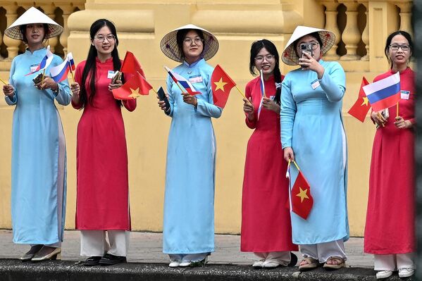 زنانی که لباس‌های سنتی ویتنامی &quot;آئو دای&quot; را پوشیده‌اند، پرچم‌های ملی ویتنام و روسیه را در حالی که منتظر ورود ولادیمیر پوتین، رئیس‌جمهور روسیه در نزدیکی کاخ ریاست‌جمهوری در هانوی در 20 ژوئن 2024 هستند، تکان می‌دهند. - اسپوتنیک ایران  