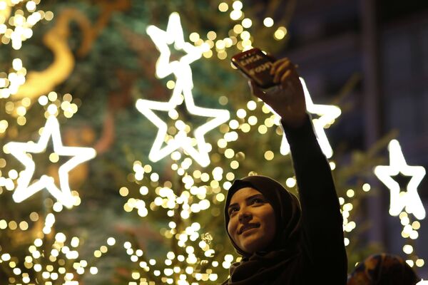 زن مسلمان لبنانی در برابر درخت کاج کریسمس در مرکز بیروت عکس سلفی می گیرد. - اسپوتنیک ایران  