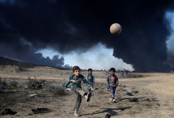پسربچه ها در حال توب بازی در  جنوب موصل در زمینه  دود  نفت در حال سوخت - اسپوتنیک ایران  