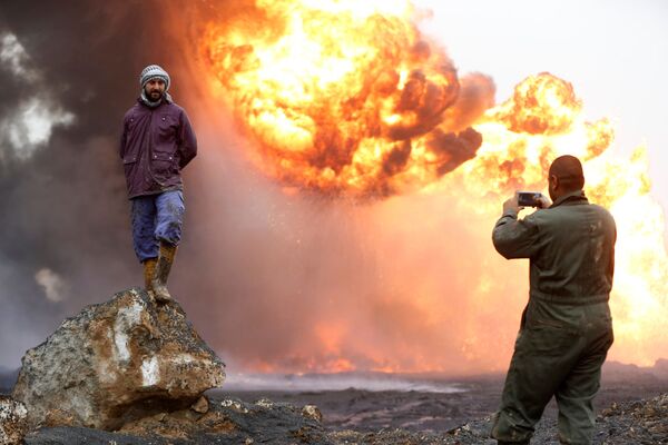 مردی در حال عکس گرفتن از دوستش  در زمینه  چاه  آتشین نفت   که توسط شبه نظاماین « داعش»  در عراق به آتش کشیده شد - اسپوتنیک ایران  