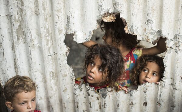 کودکان فلسطینی در حال تماشا از یک حفره که بر روی حصار ایجاد شده - اسپوتنیک ایران  