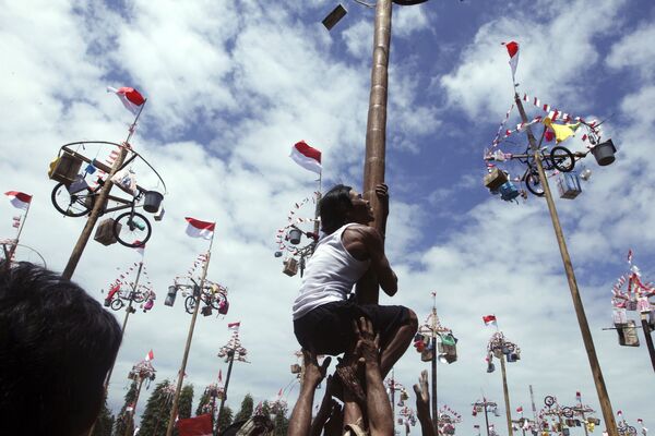 مردی در حال تلاش برای بالارفتن از ستون تا جایزه دوچرخه را در جشن روز استقلال در بالی اندونزی بدست بیاورد - اسپوتنیک ایران  