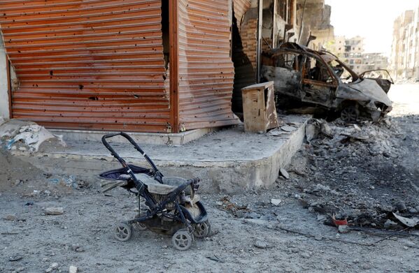 کالسکه کودک در کنار یک خودروی سوخته در شهر رقه - سوریه - اسپوتنیک ایران  