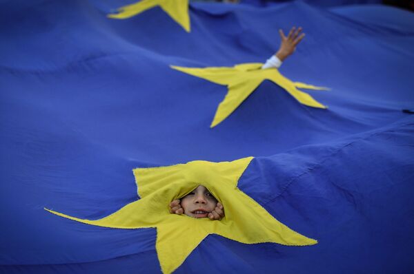 پسربچه ای از لای پرچم اتحادیه اروپا به تظاهرات در بخارست نگاه می کند - اسپوتنیک ایران  