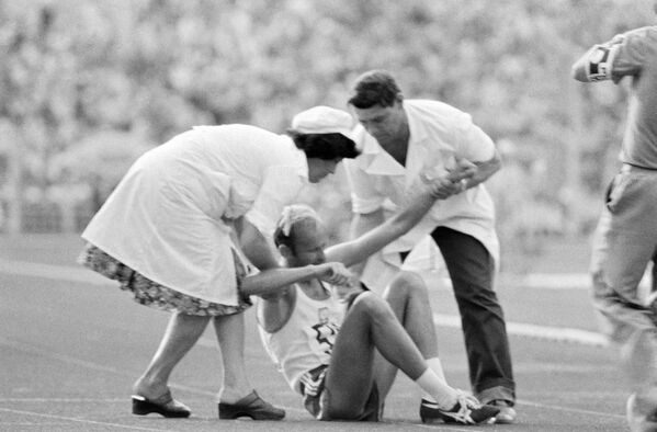 پزشکان به ورزشکار دو و میدانی به خاطر آسیب دیدگی اش حین مسابقه کمک می کنند، بازی های المپیک، سال ۱۹۸۰ - اسپوتنیک ایران  