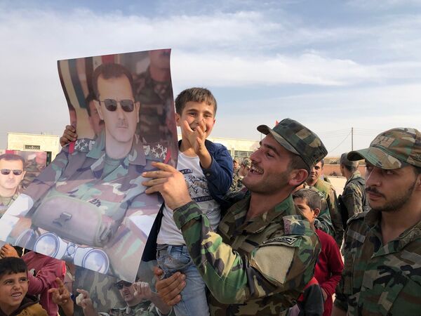 کودکان و پرسنل ارتش که پوسترهایی با پرتره بشار اسد، رئیس جمهور سوریه در شهر منبج - اسپوتنیک ایران  