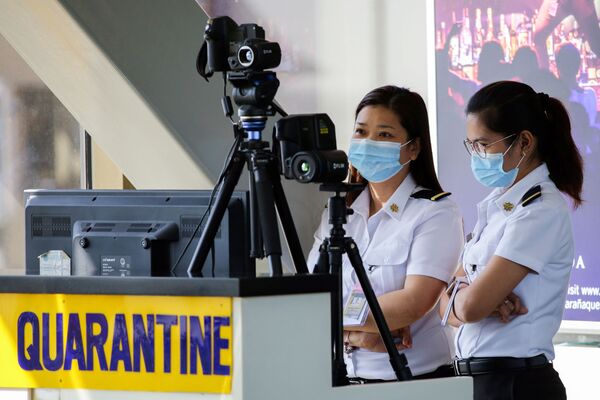 ماموران فرودگاه نینو آکینو در فیلیپین که صورت خود را با ماسک پوشانده اند، در پشت اسکنر گرما مراقب هستند  - اسپوتنیک ایران  