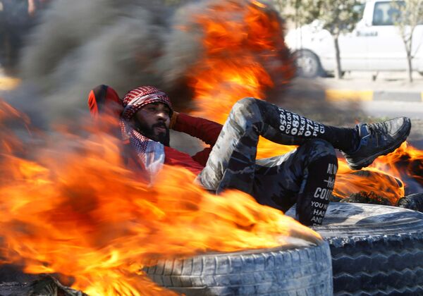 معترض در بین لاستیک های آتش گرفته که جاده را در تظاهرات در نجف عراق بسته بود - اسپوتنیک ایران  