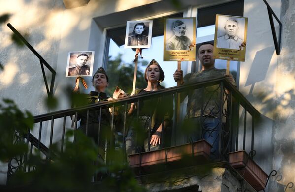 ساکنان خانه ای در سواستوپول که عکس بستگانشان که در جنگ جهانی دوم شرکت کرده بودند را در دست گرفته و سرود پیروزی می خوانند. - اسپوتنیک ایران  