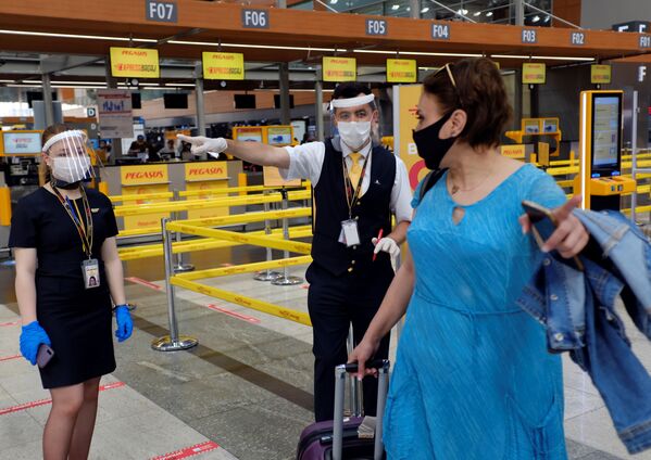 کارکنان شرکت هوایی پگاسوس ایرلاین با ماسک به مسافر مسیرش را در فرودگاه بین المللی استانبول نشان می دهند - اسپوتنیک ایران  